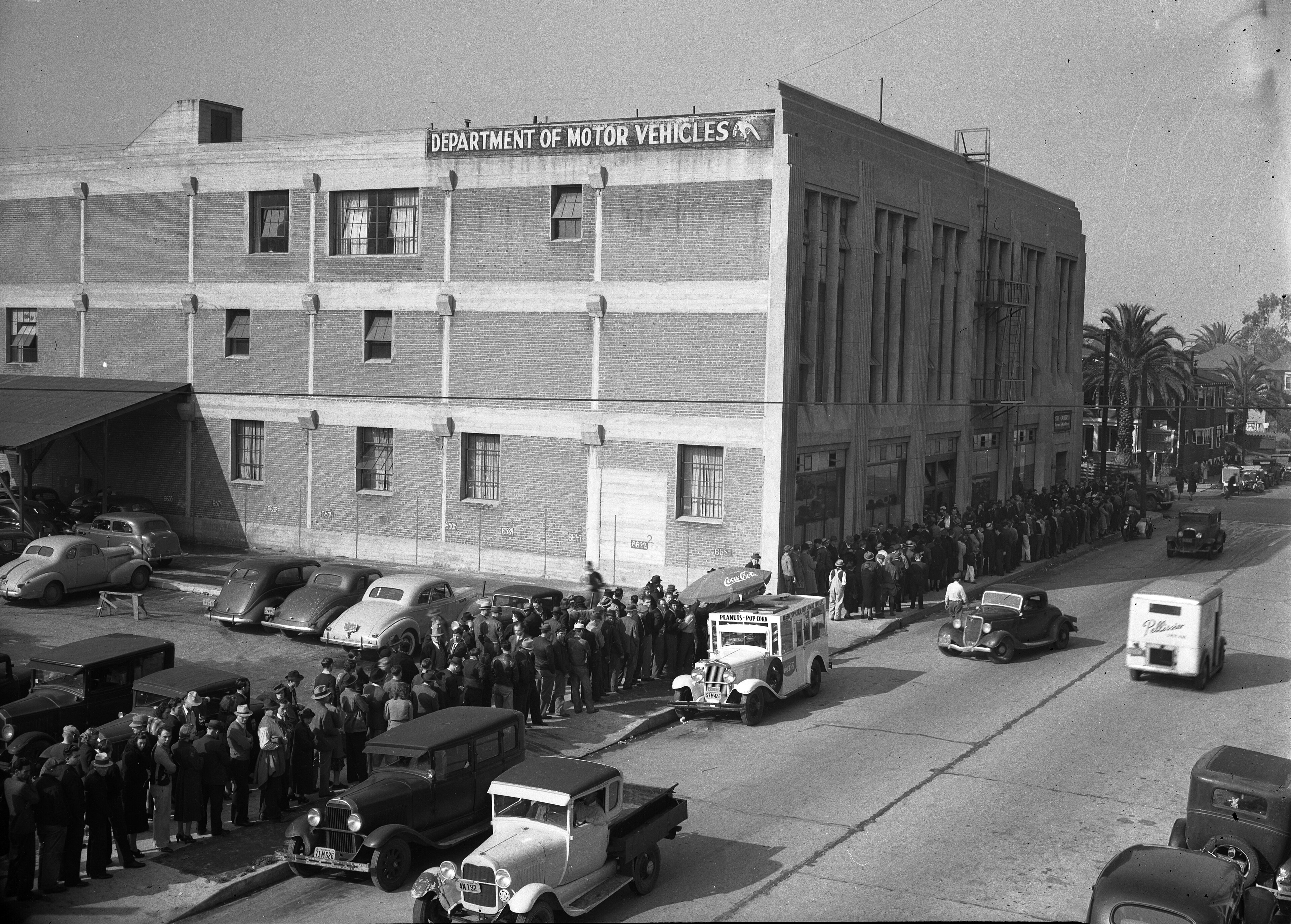 A 1940 building under a sign reading Department of Motor Vehicles, with a long queue of people down the street