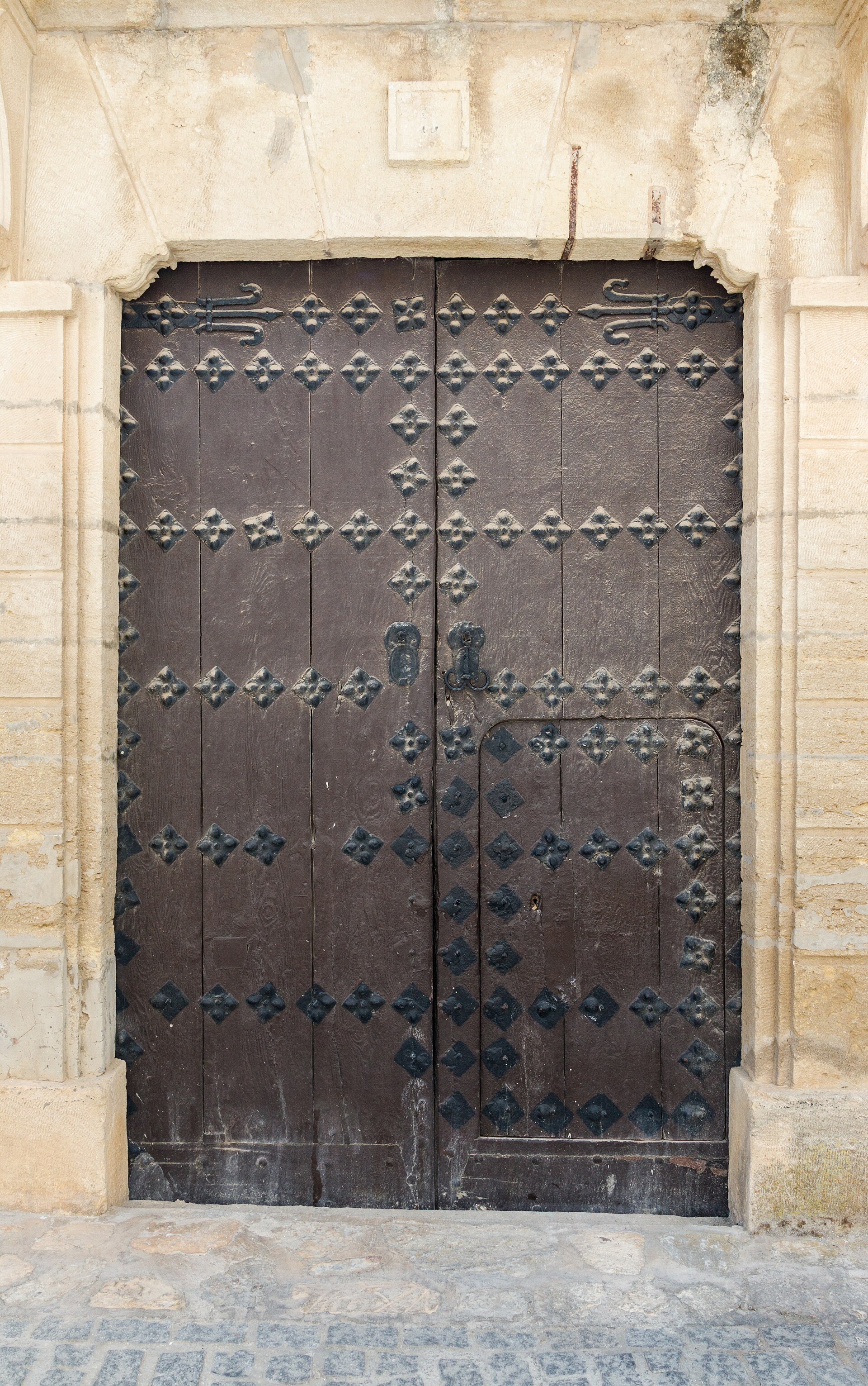 A heavy studded wooden double door, closed, in a stone frame